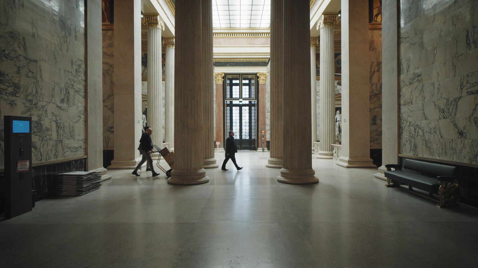 Säulenhalle im Parlament, zwei Männer schieben Kisten vorbei